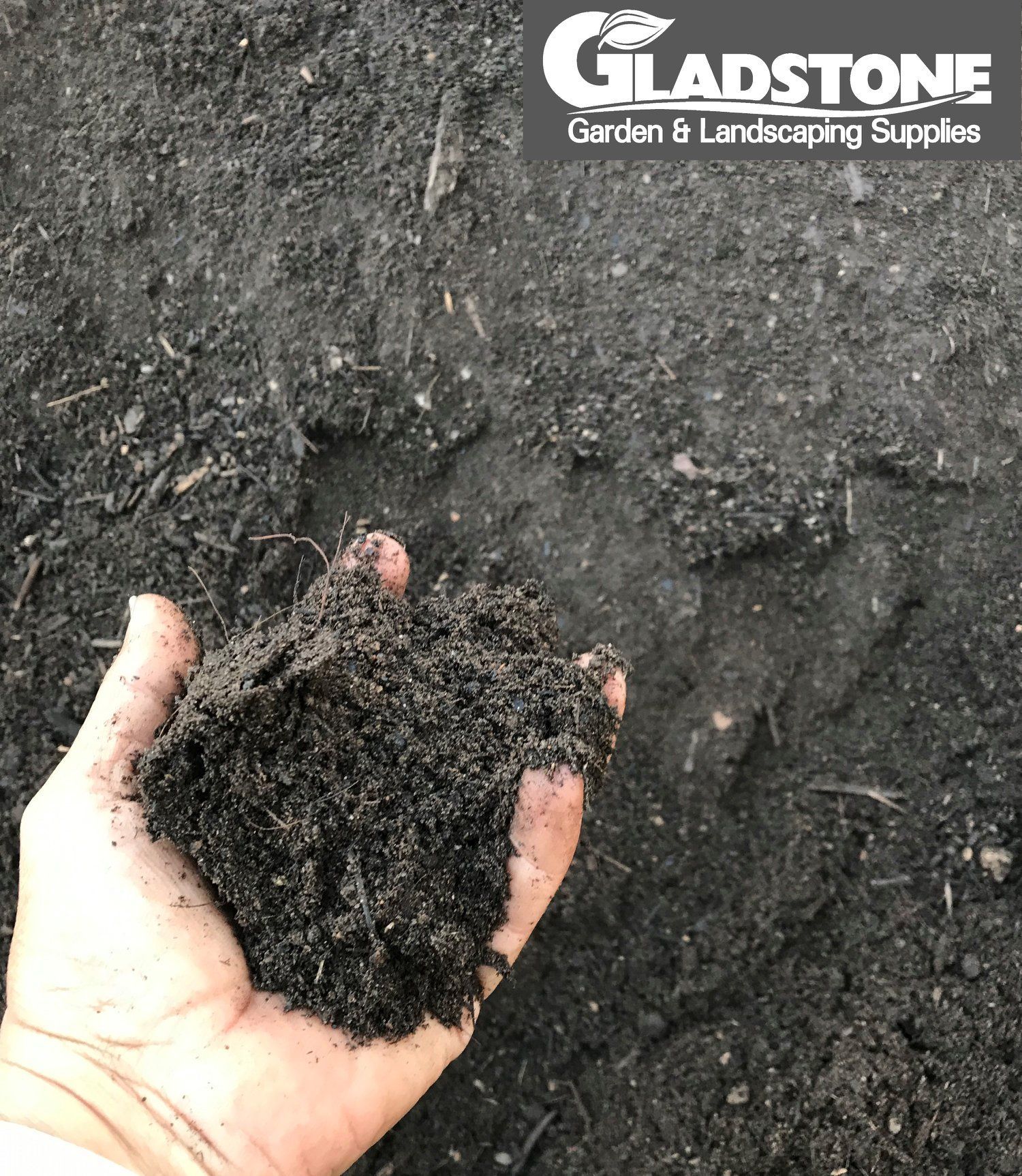 Hand Holding a Pile of Dark Soil, Gladstone Garden & Landscaping Supplies Logo in The Corner — Gladstone Garden & Landscaping Supplies In Burua, QLD
