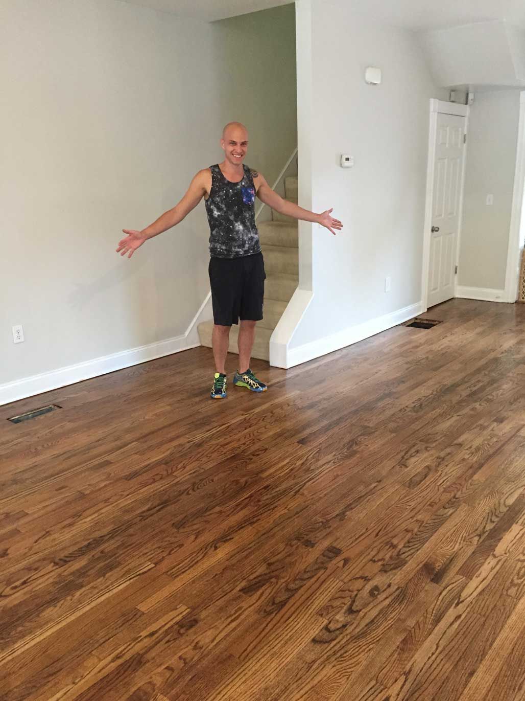 A man is standing in an empty room with his arms outstretched.