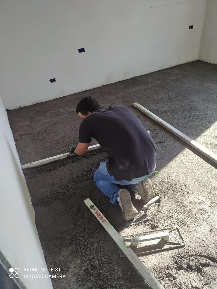 Un uomo è inginocchiato in una stanza mentre stende il cemento sul pavimento.