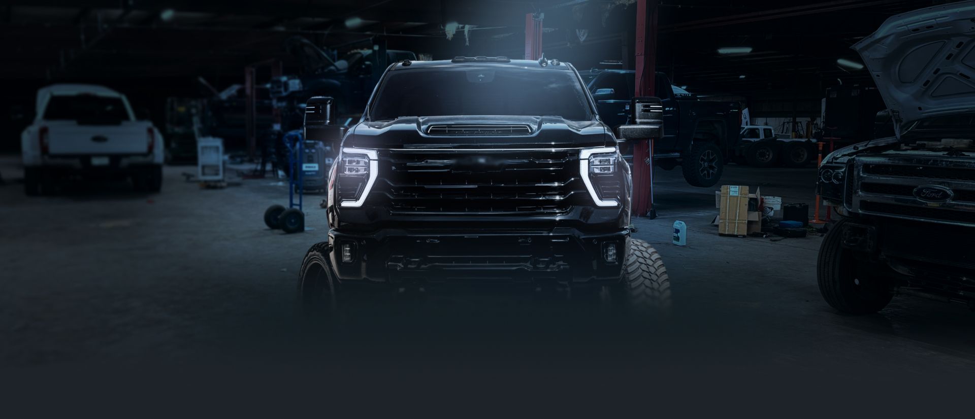 A large, black truck with bright headlights is centered in a dimly lit garage. | Bad Habit Motorsports LLC