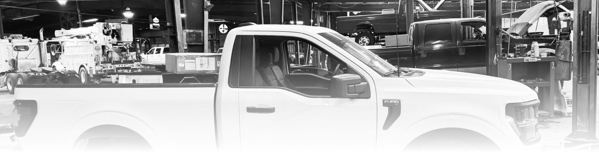 A white pickup truck parked in a garage with other vehicles and equipment visible in the background. | Bad Habit Motorsports LLC