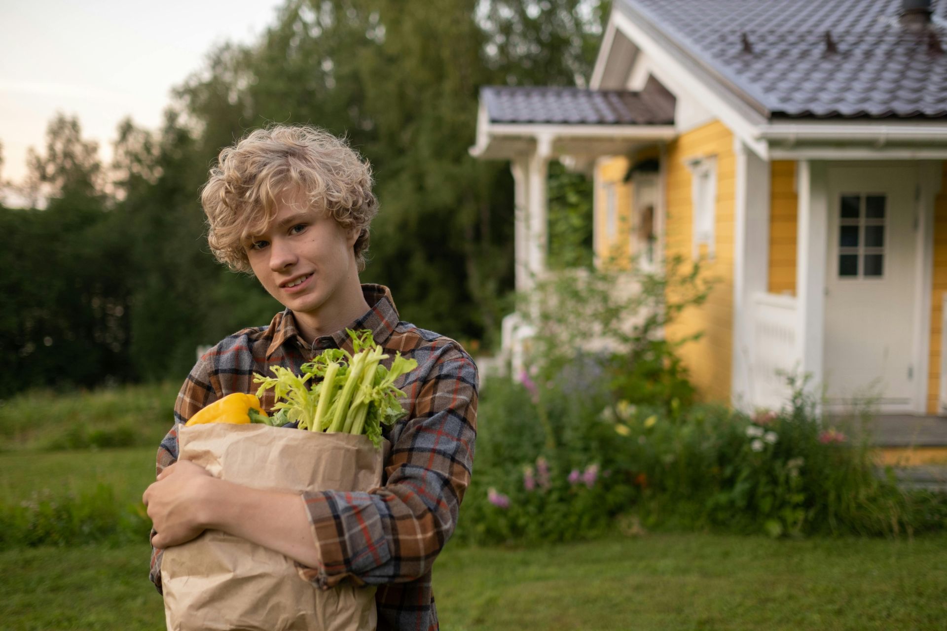 A young man is holding a bag of vegetables in front of a house.