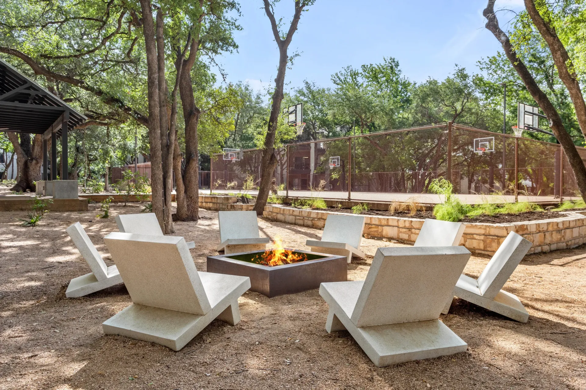Outdoor fire pit with lounge chairs and a basketball court in the background.