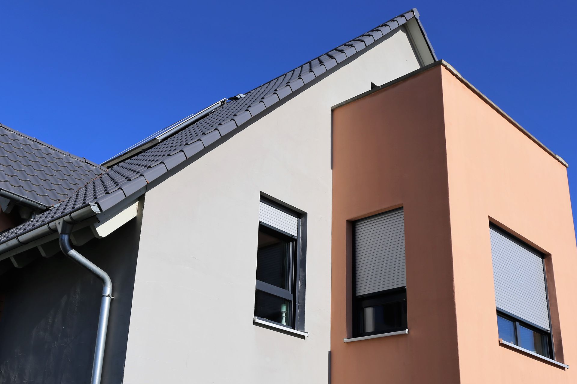 A modern two-story home exterior with a gabled roof, white and tan stucco walls, and windows with gray shutters.
