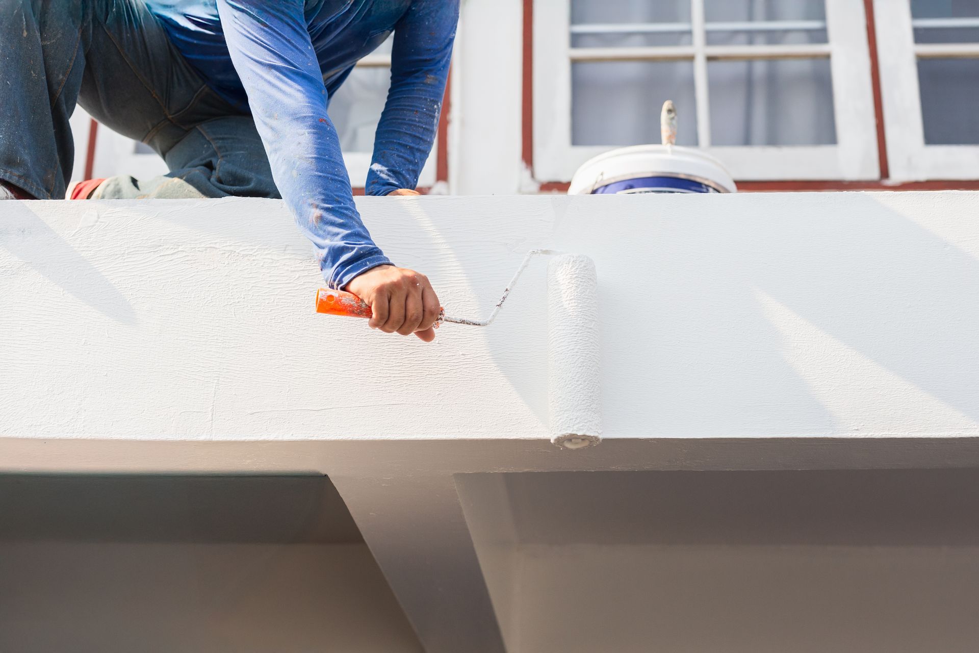 A person uses a paint roller to apply white paint to the exterior wall of a building.