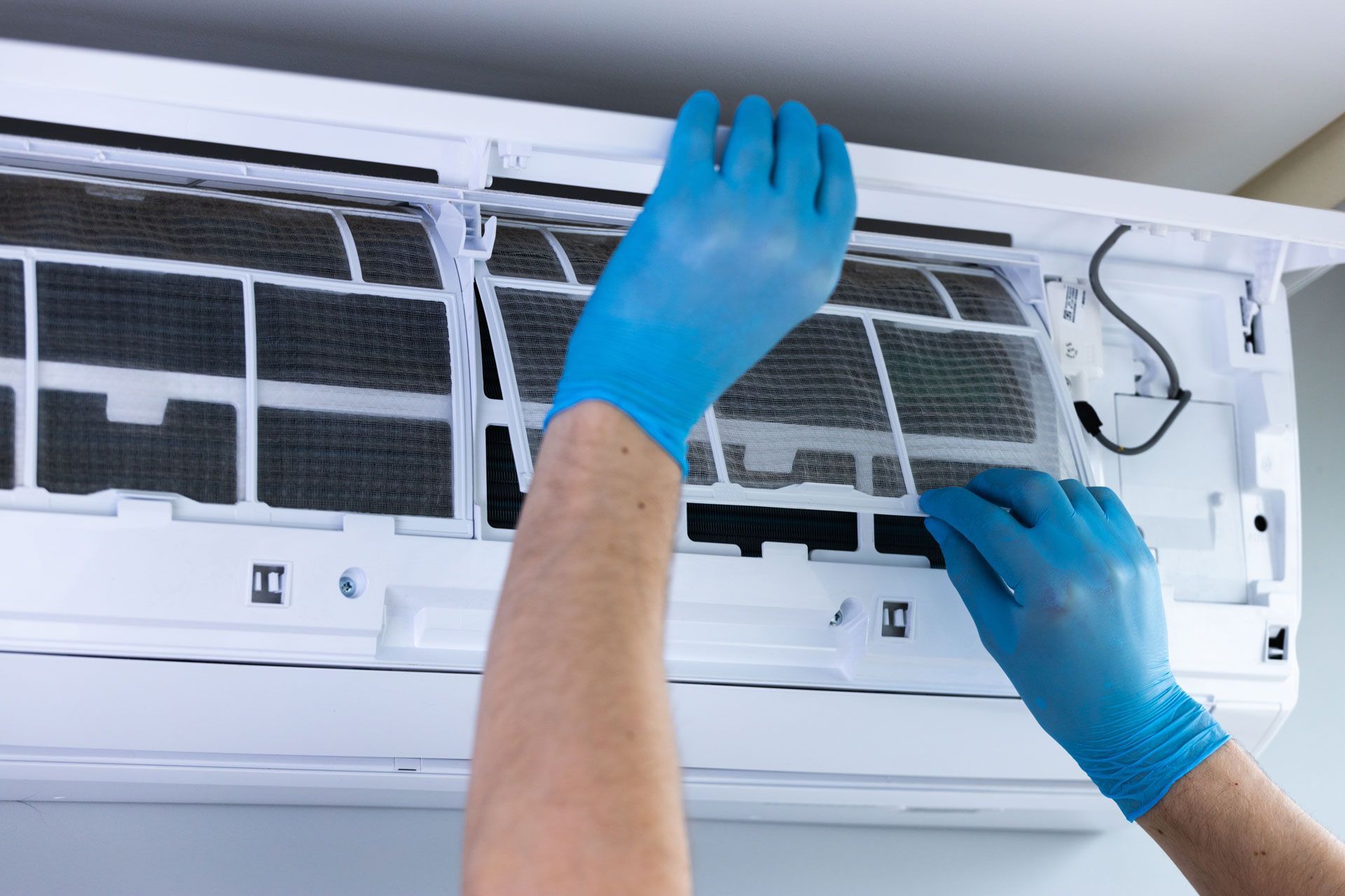 Hands in blue gloves cleaning an indoor air conditioner filter unit