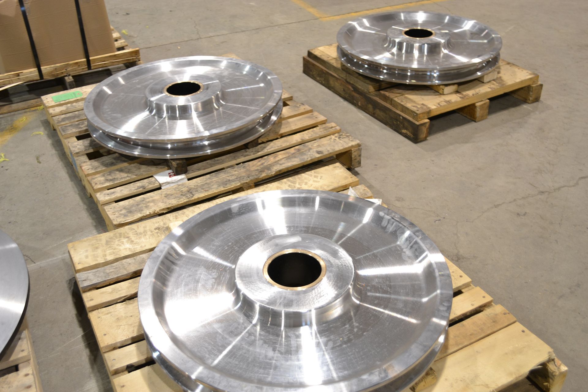 Four large, shiny metal wheels on wooden pallets in a factory setting.