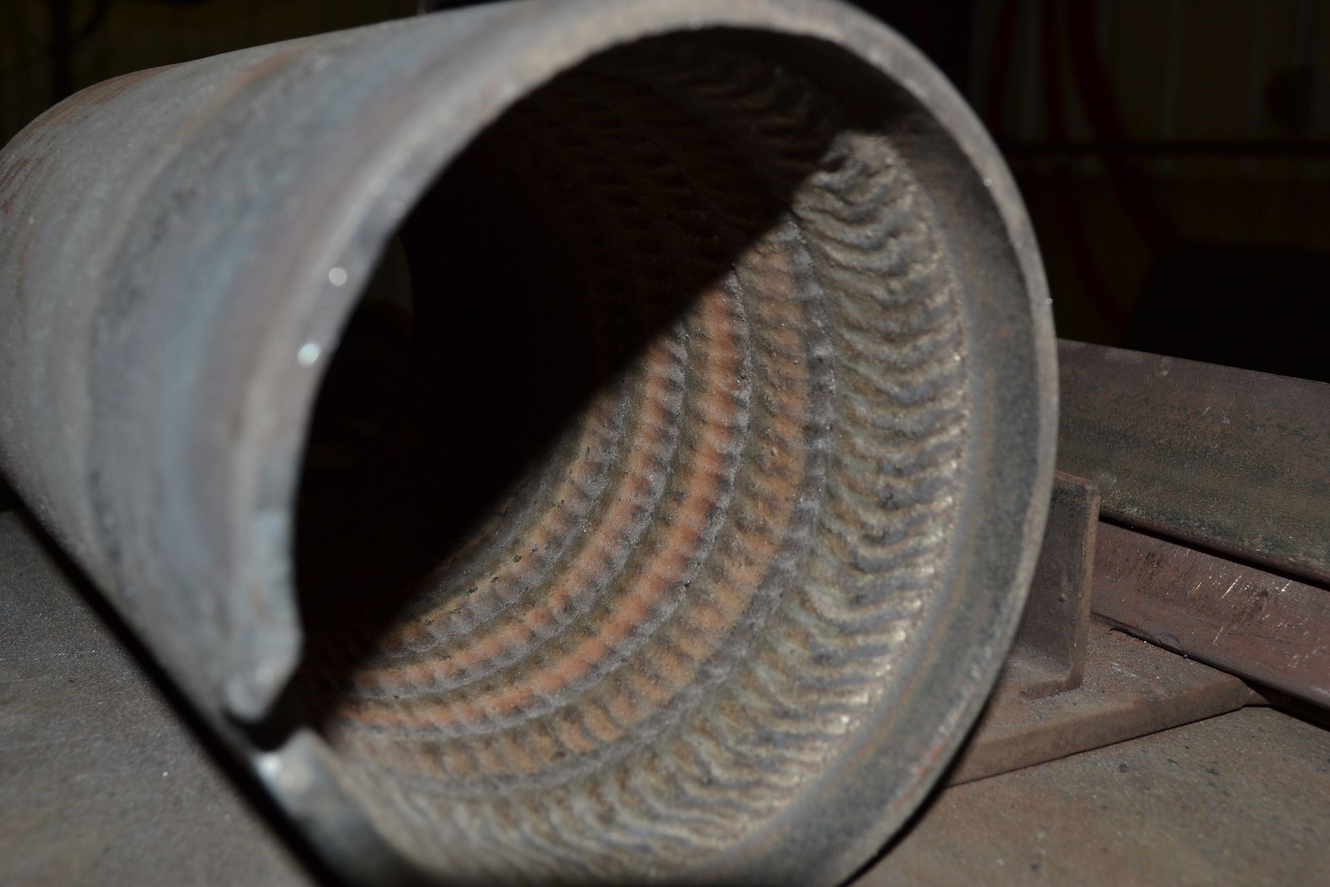 Inside view of a steel pipe revealing a spiral pattern of welded seams, resting on a surface.
