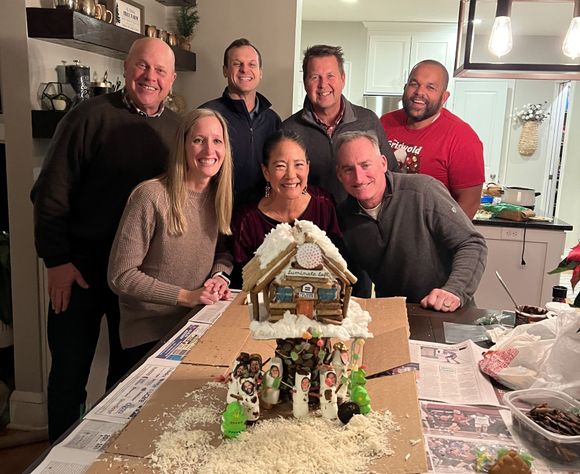 A group of people are posing for a picture in front of a gingerbread house.