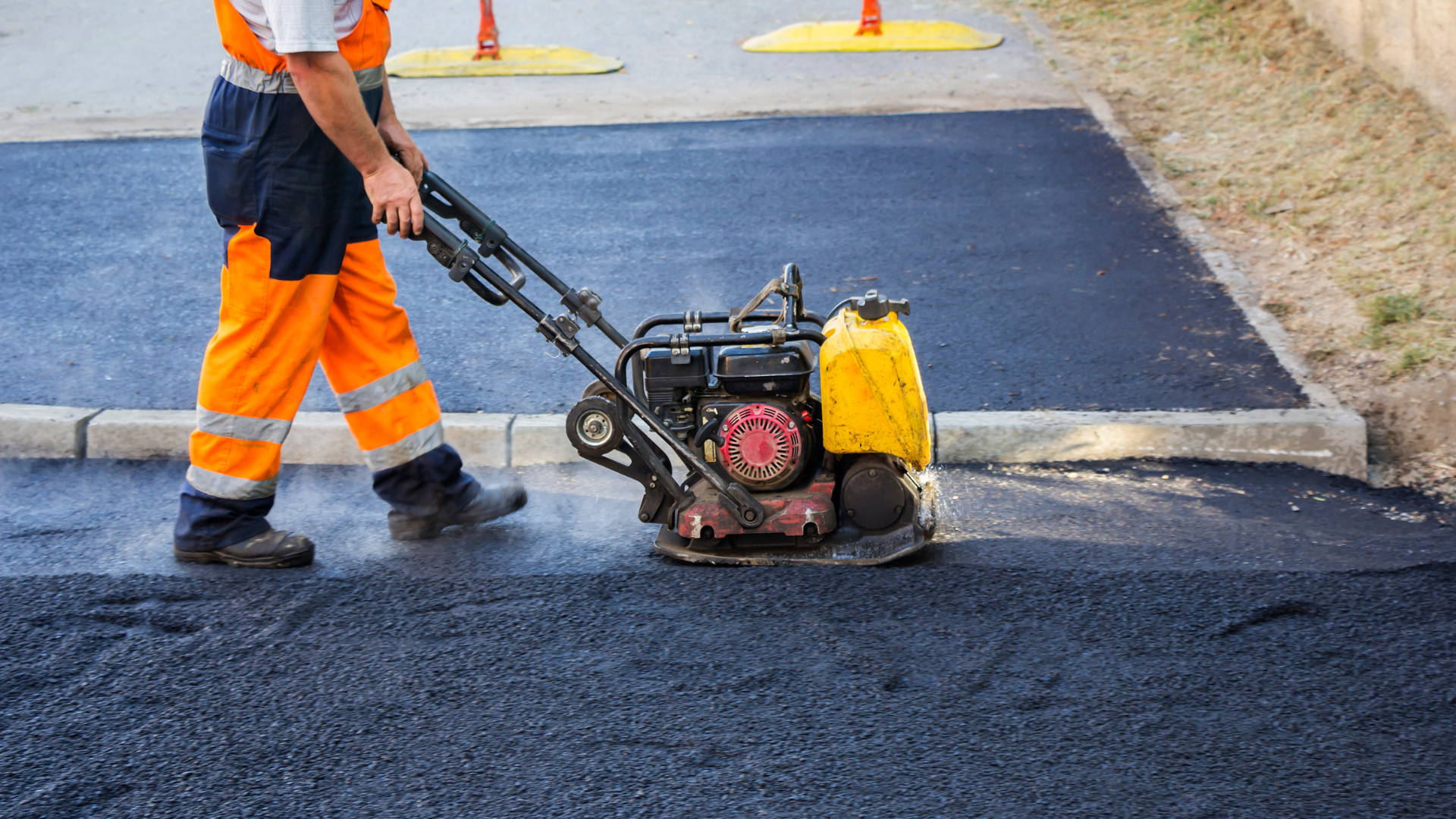 A man is using a machine to compact asphalt on a road.
