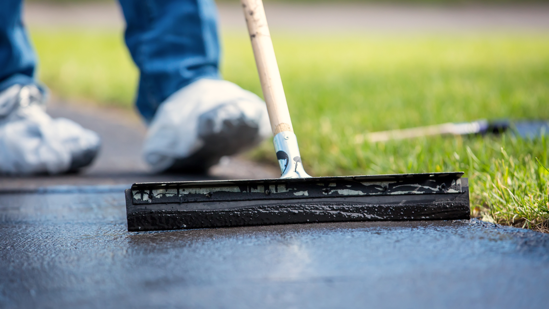 A person is using a broom to spread asphalt on a sidewalk.
