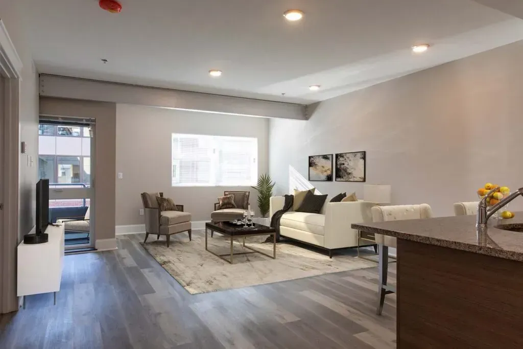 Modern living room with a white sofa, two armchairs, a coffee table, and a rug. Gray walls and flooring.