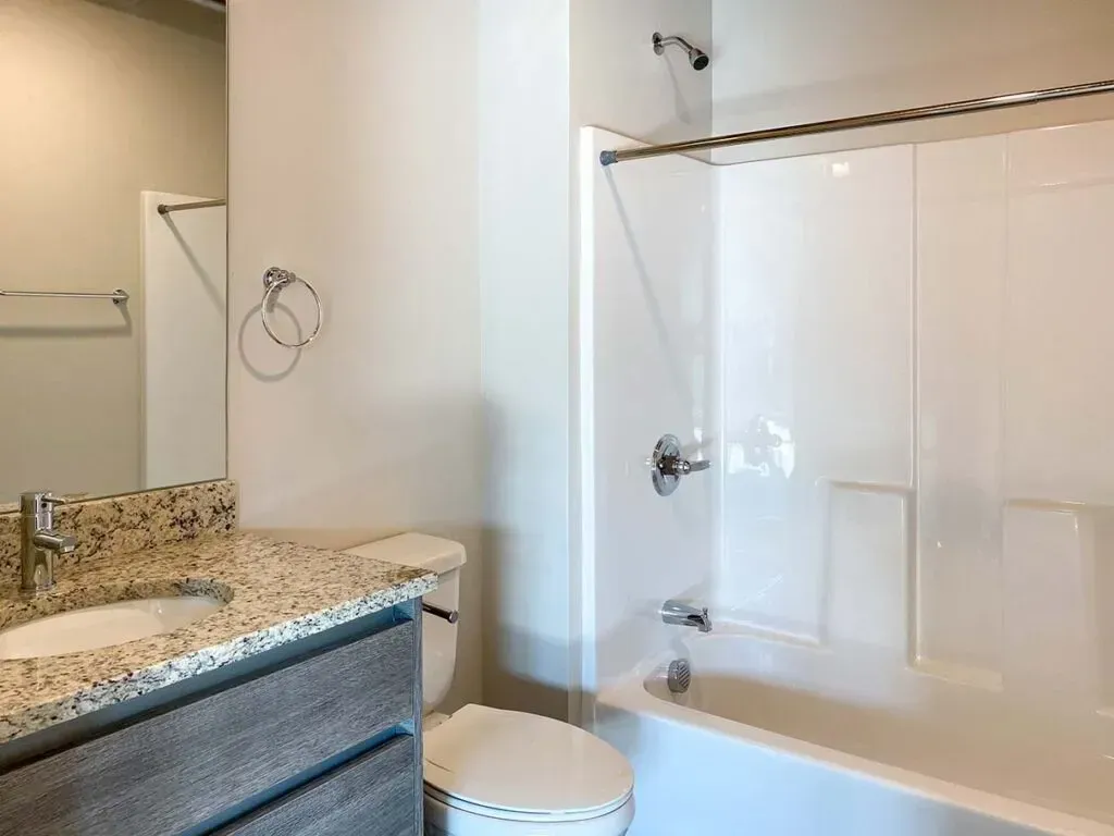 Bathroom with a white bathtub, toilet, and vanity with granite countertop.
