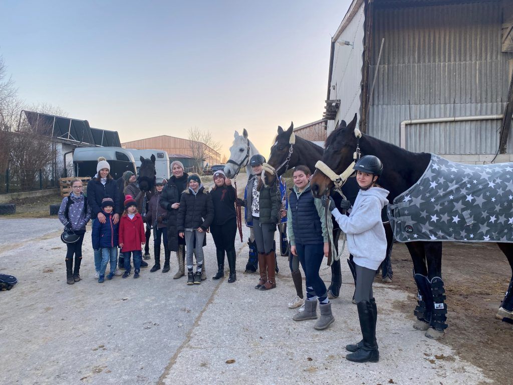 Eine Gruppe von Kindern und Erwachsenen steht mit Pferden vor einem Stall.