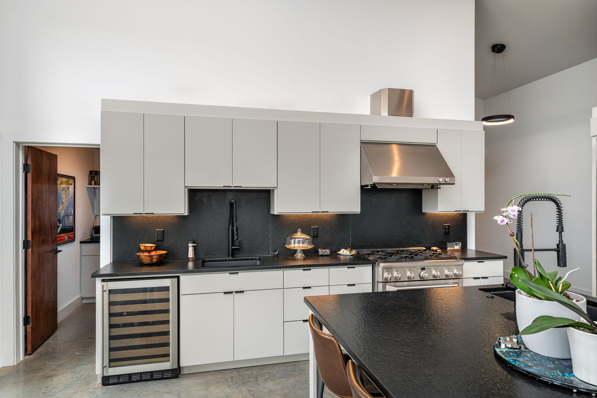 A kitchen with white cabinets , black counter tops , stainless steel appliances and a wine cooler.