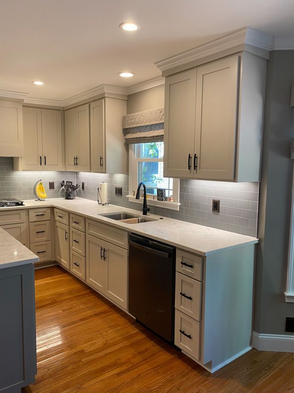 A kitchen with white cabinets , a sink , a dishwasher and a window.