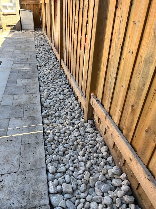 A wooden fence surrounded by rocks next to a sidewalk.