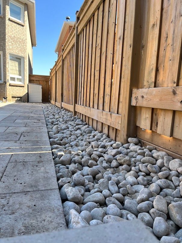 A wooden fence is surrounded by rocks and a sidewalk.
