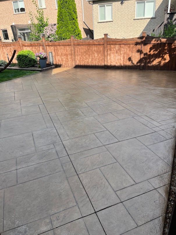 A concrete patio with a wooden fence and a house in the background.