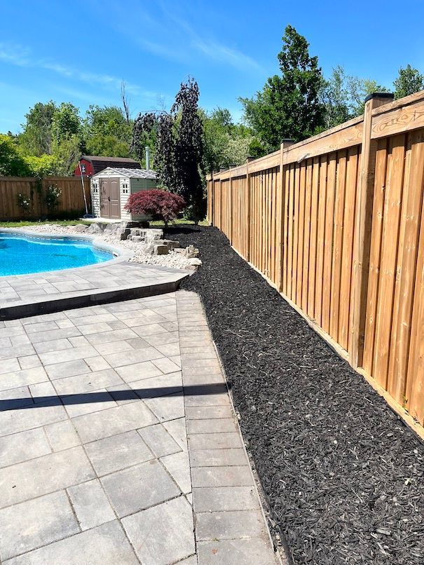 A wooden fence surrounds a swimming pool in a backyard.