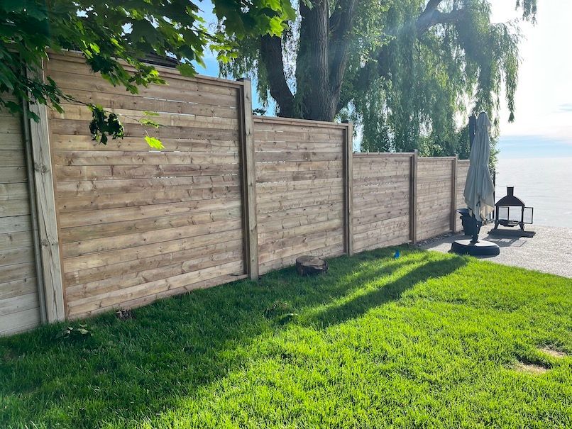 A wooden fence surrounds a lush green lawn next to a body of water.