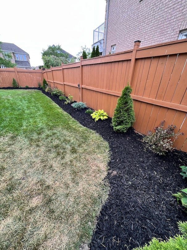 A backyard with a wooden fence and black mulch.