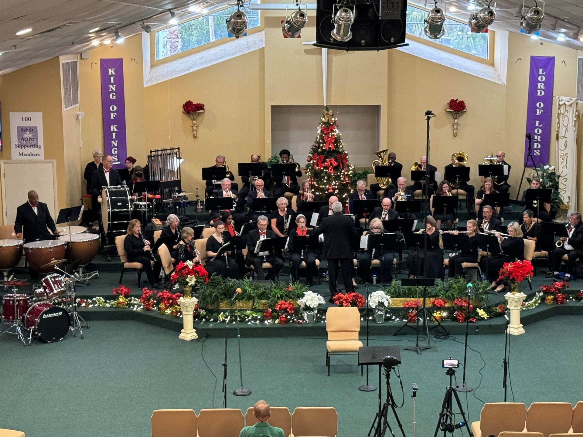 A large choir is performing in a church with a christmas tree in the background