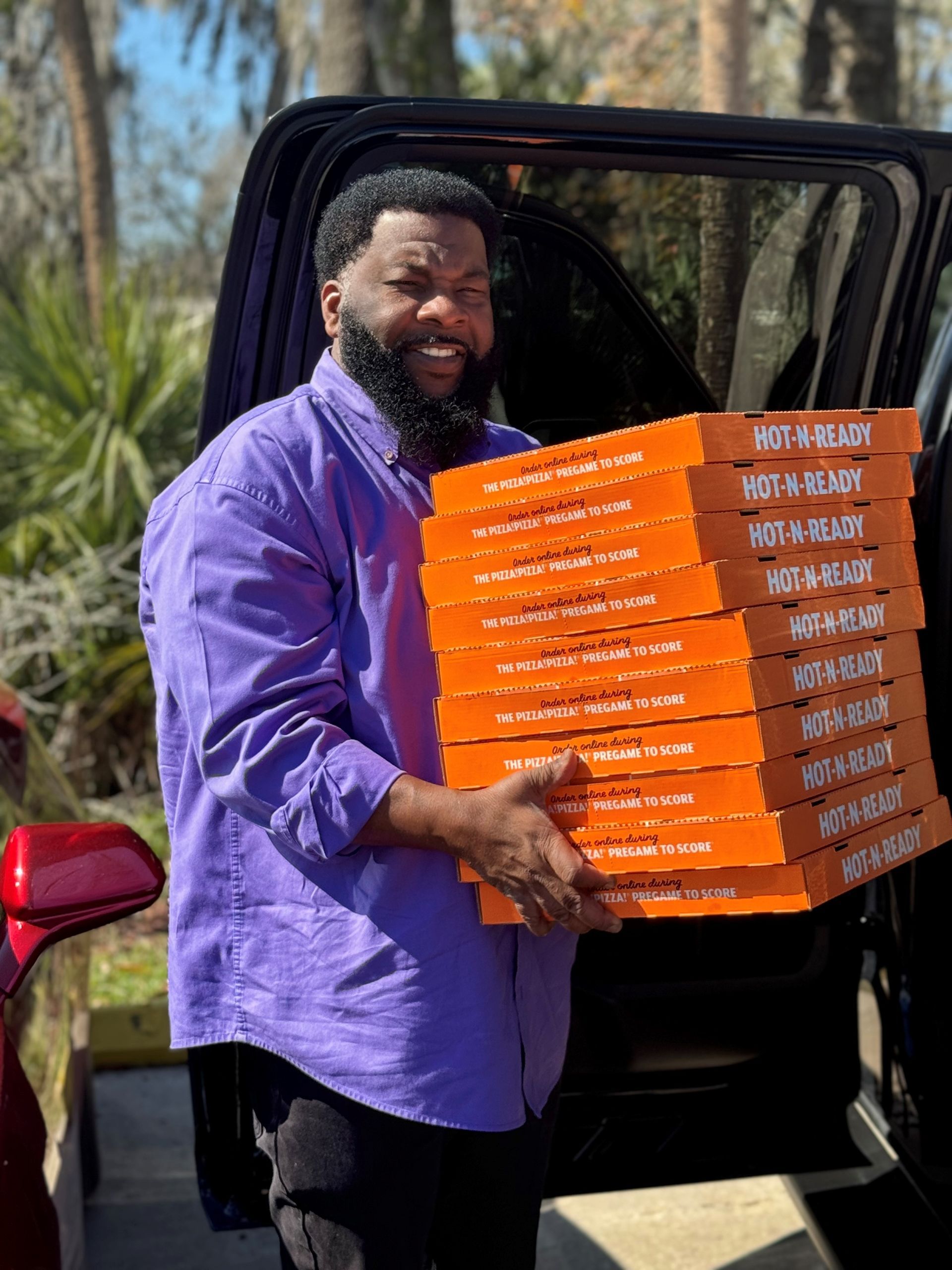 A man in a purple shirt is carrying a stack of pizza boxes