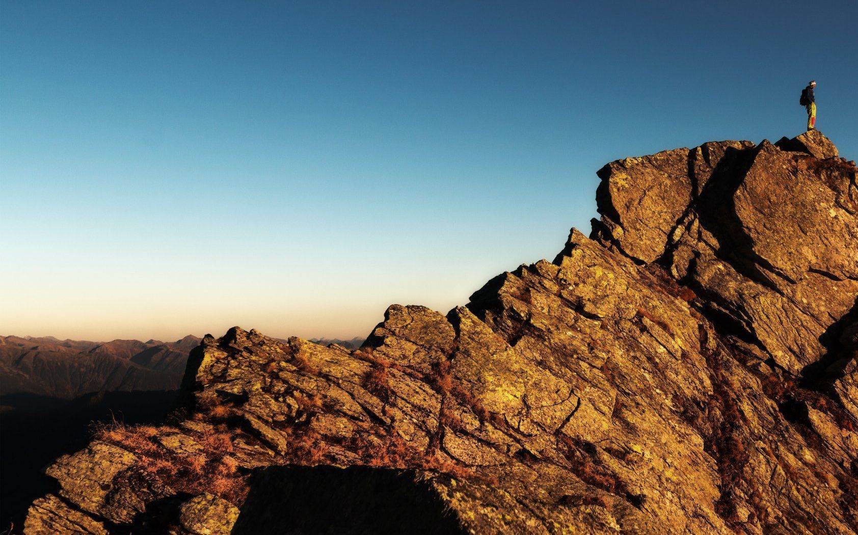 A person standing on top of a rocky mountain with a cross