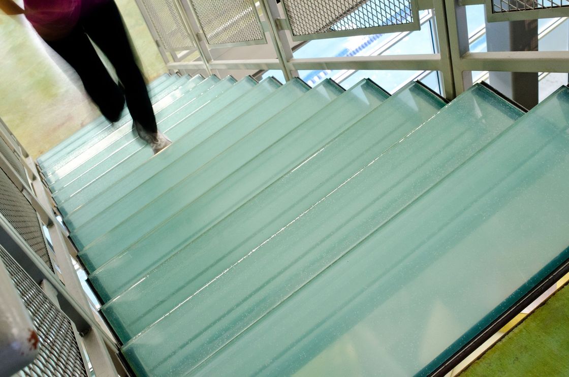 Person descends a staircase with transparent glass steps and metal supports.