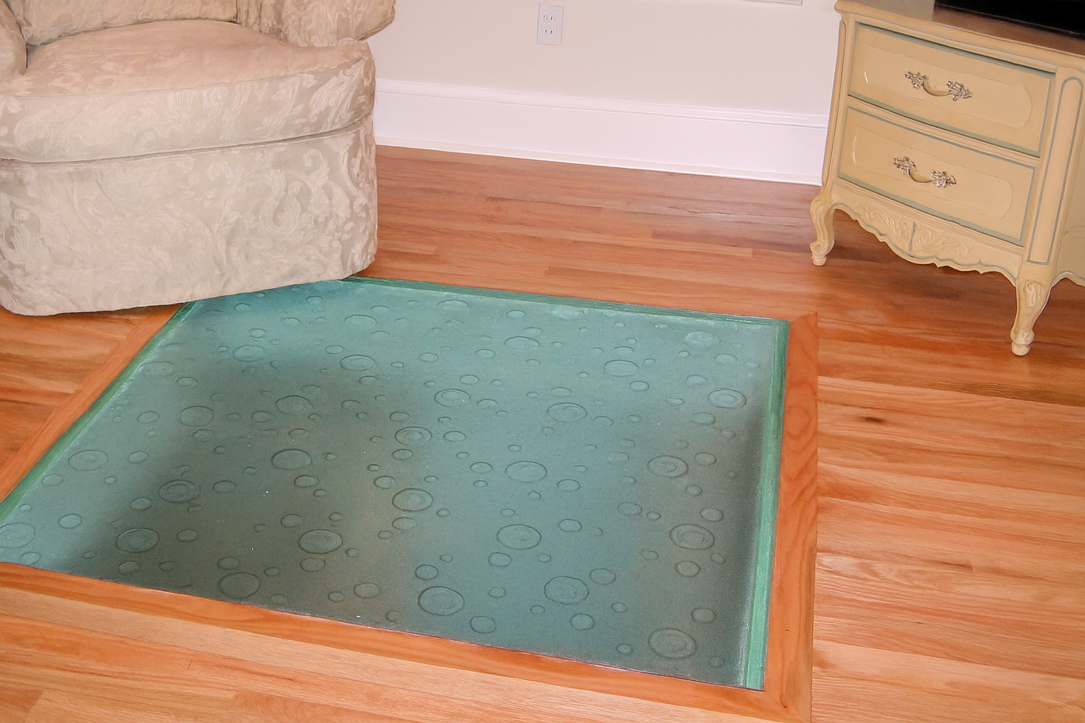 A square of teal-colored glass in a wooden floor, surrounded by wooden trim.