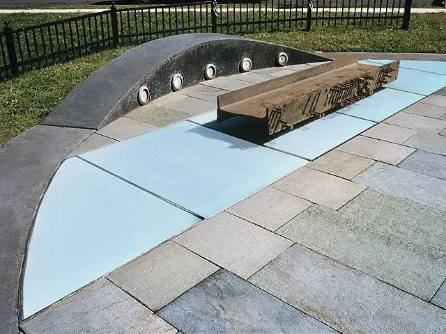 Stone plaza with arch, light-colored tiles, and a bronze sculpture. 9/11 memorial glass floor