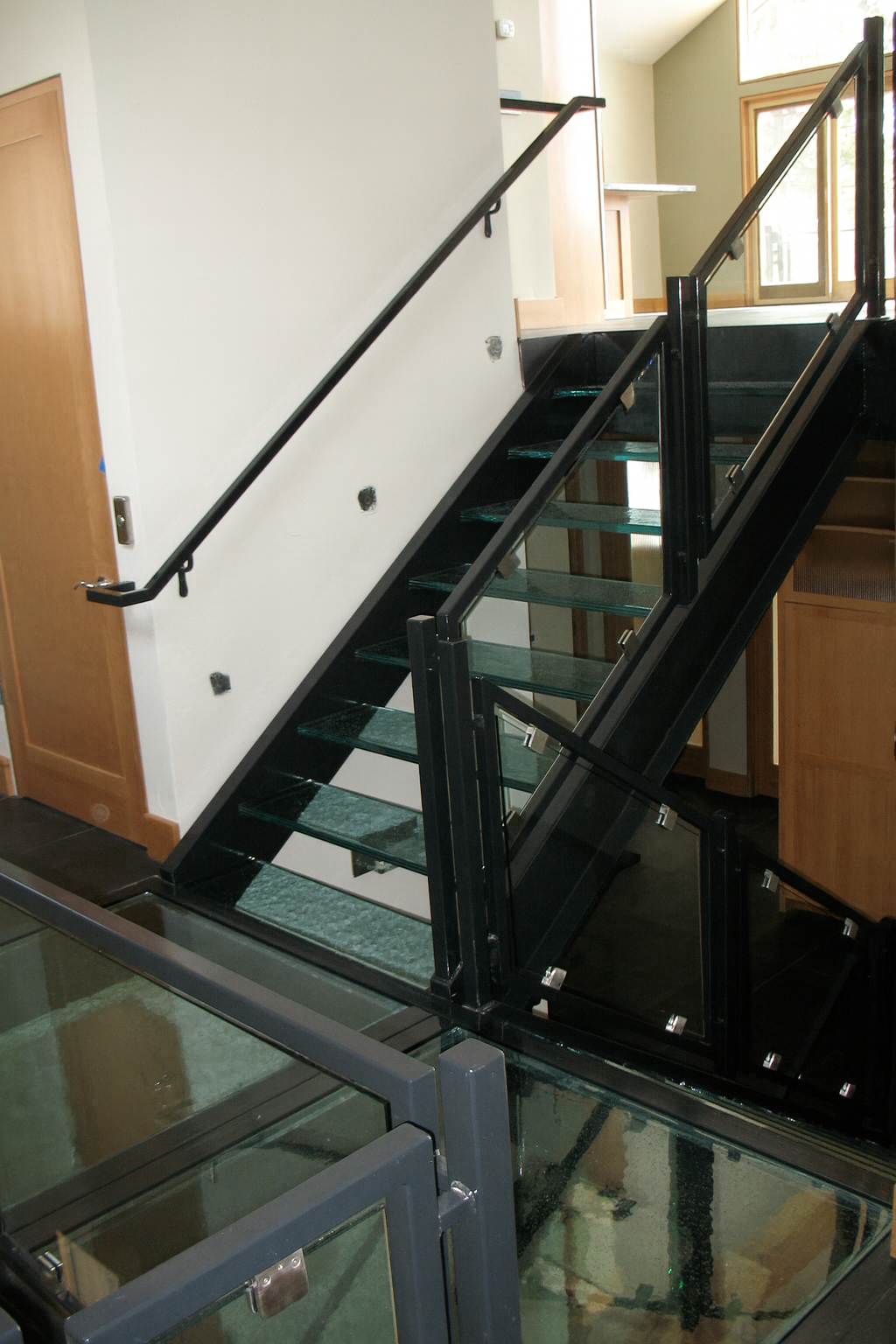A black metal staircase with glass steps and railings in a modern interior setting.