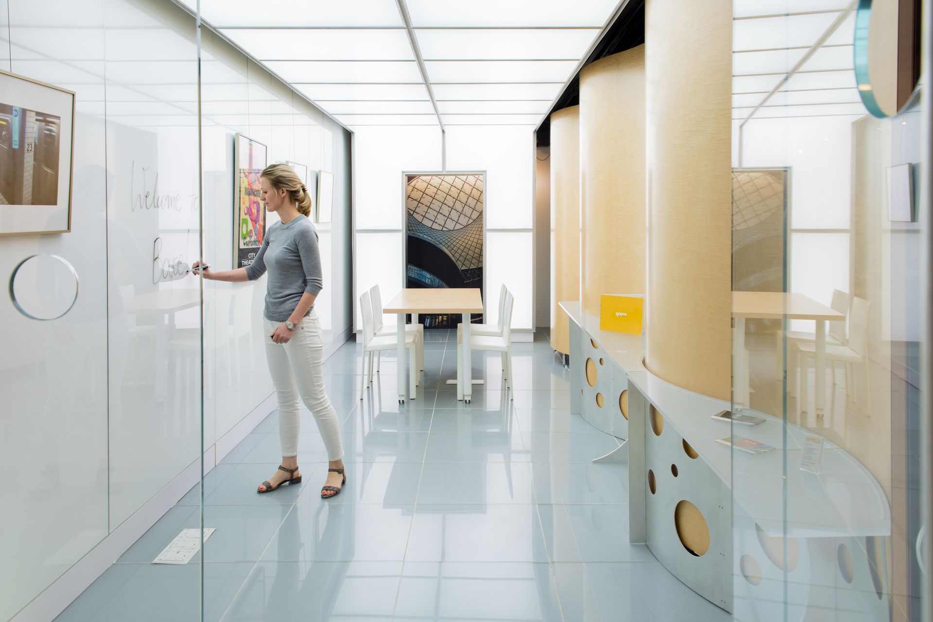 Woman standing at a whiteboard in a modern, bright office space, writing with a marker standing on glass floors.