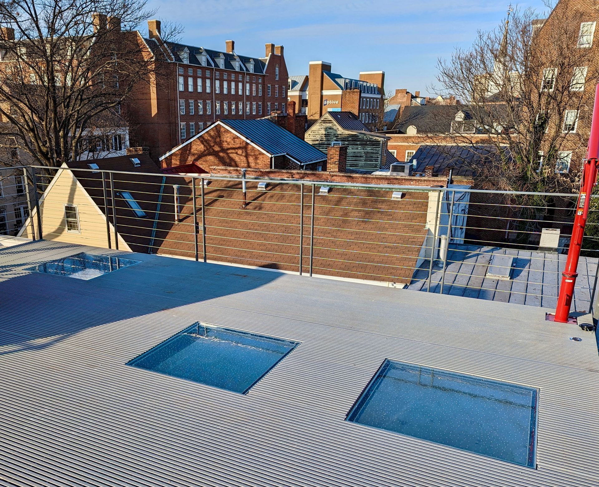 Rooftop with circular textured flooring, two skylights, and a red pole. Buildings in the background.