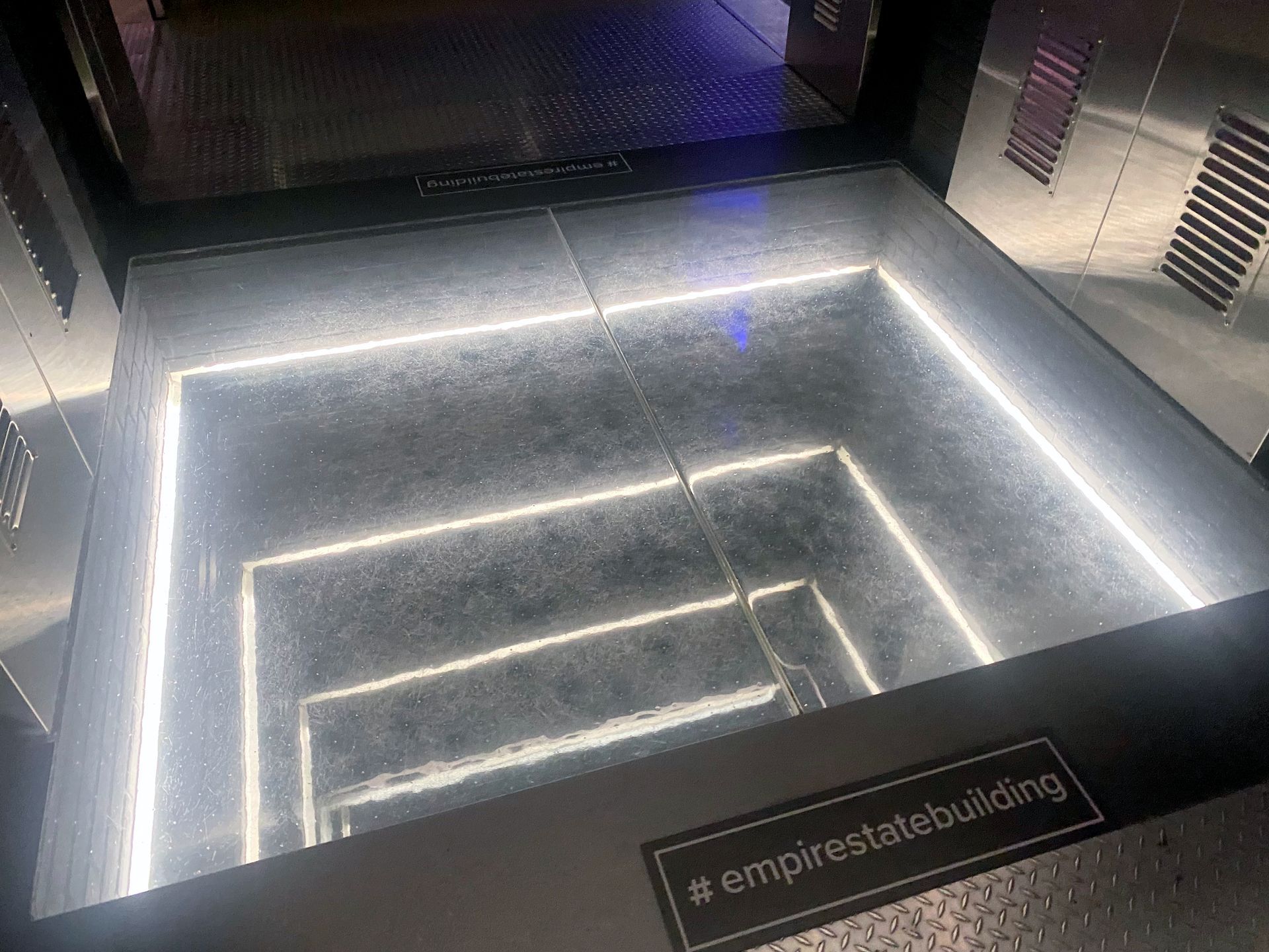 Looking down a glass floor with glowing lights, a view of the Empire State Building.