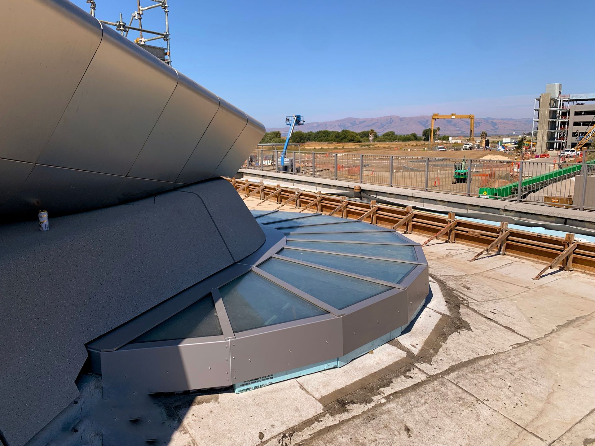 Exterior view of modern building under construction with a glass-covered section and construction site in the background.