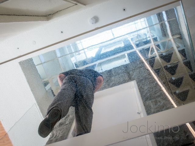 Man peering down through a glass floor into a hallway.