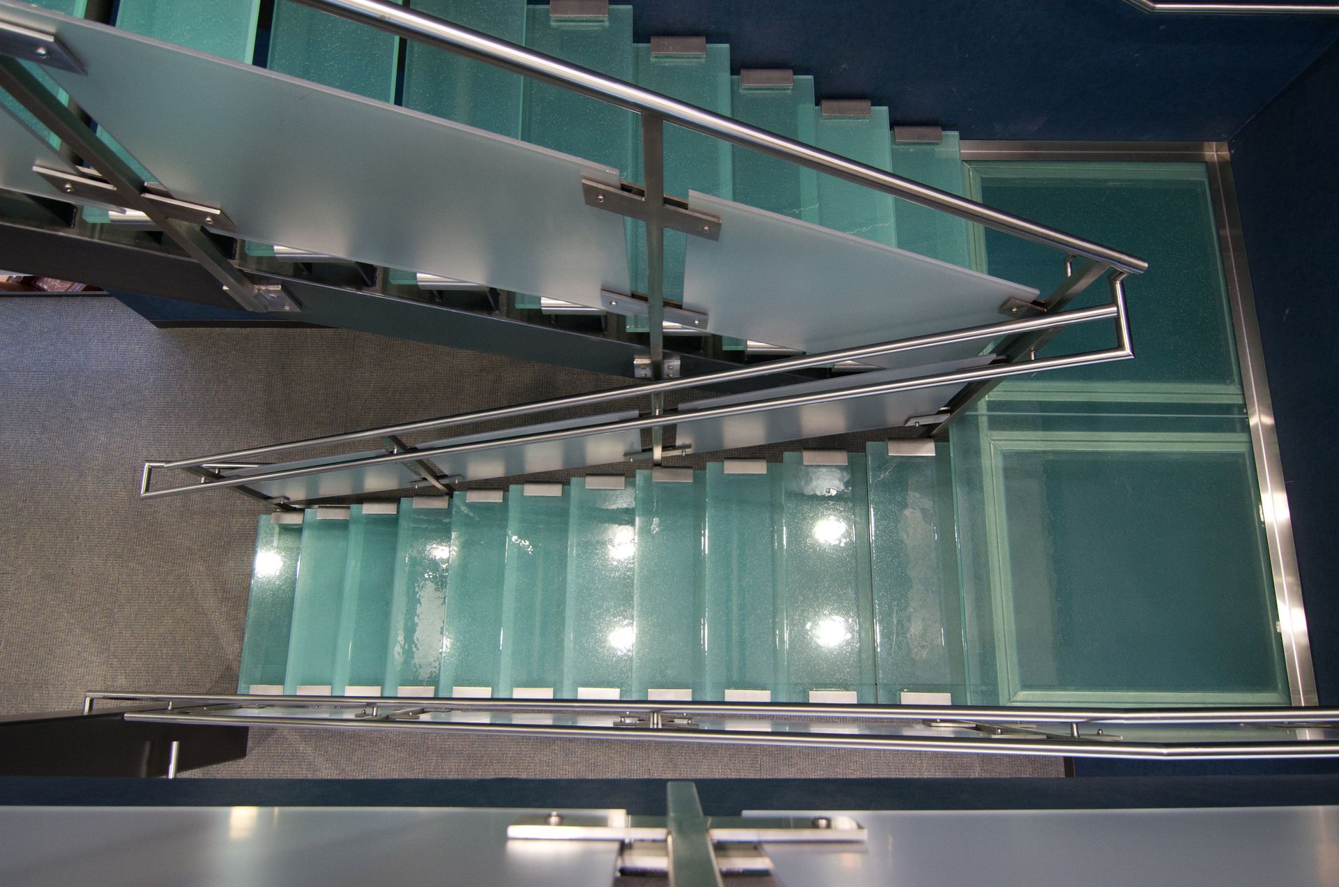 Glass staircase with metal railings, viewed from above.