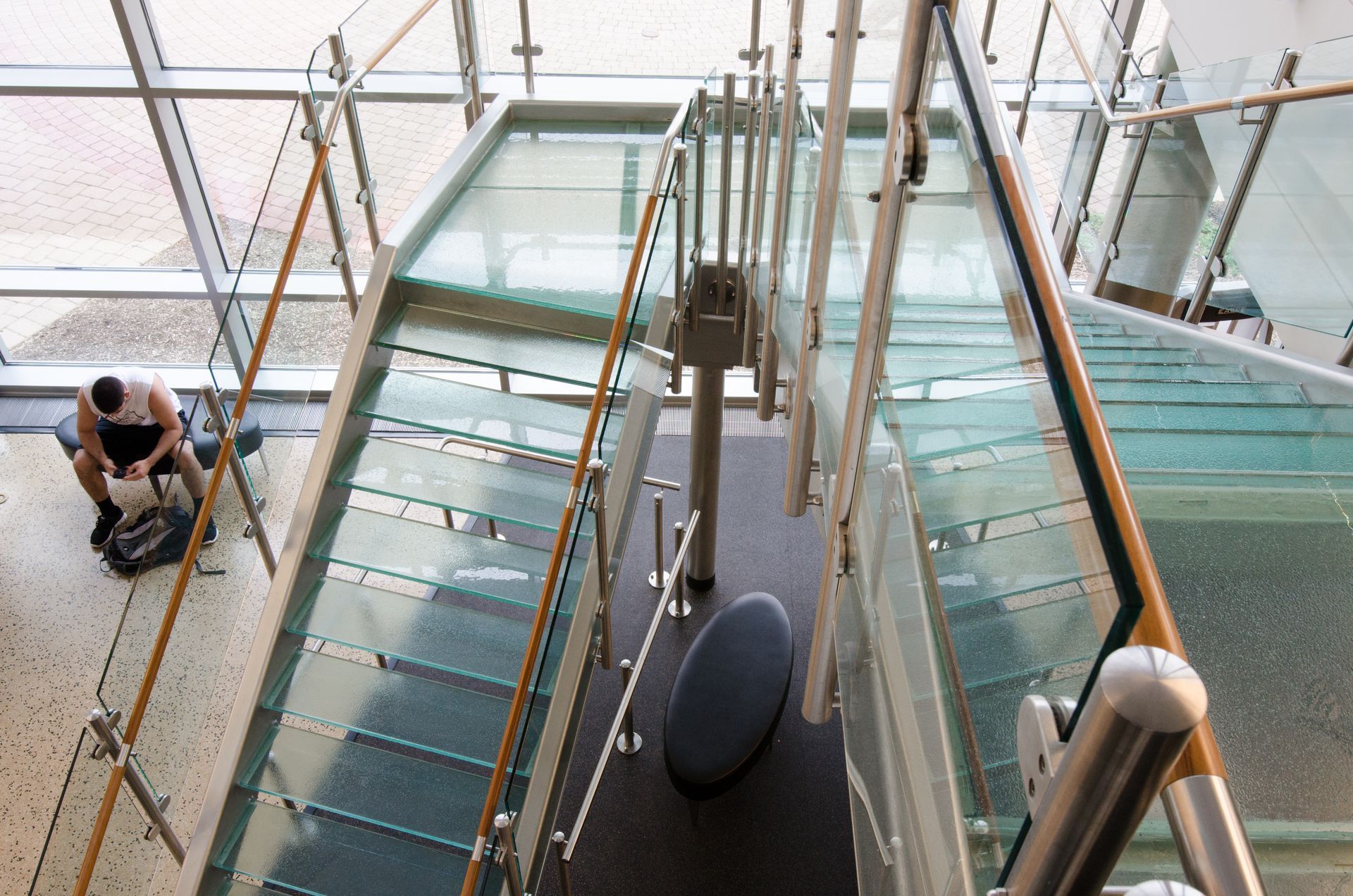 Staircase with glass steps and metal railings. Person at bottom left.