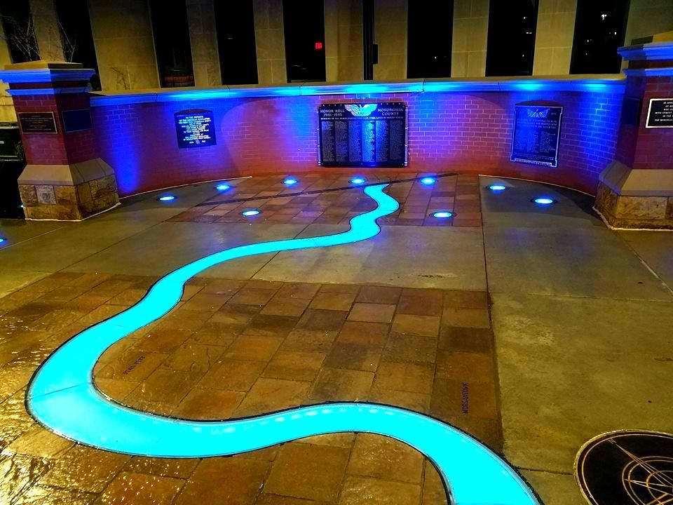 Blue-lit walkway resembling a river in front of a brick wall with plaques at night.