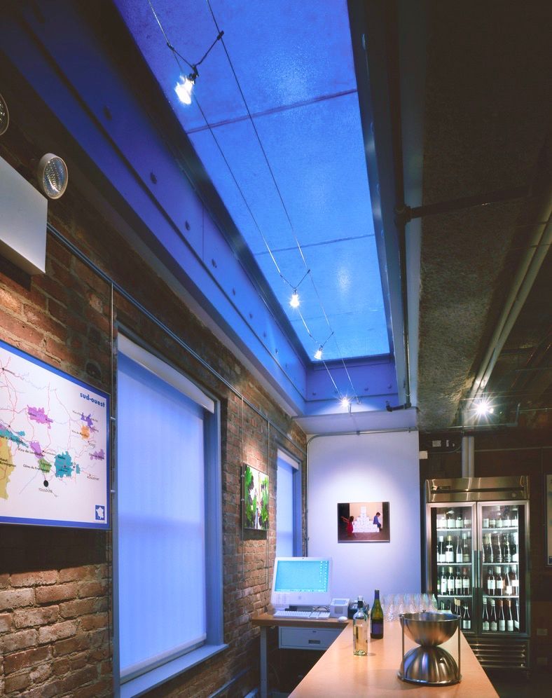 Interior view of a bar with brick walls, a long skylight with blue lighting, and a wooden bar.