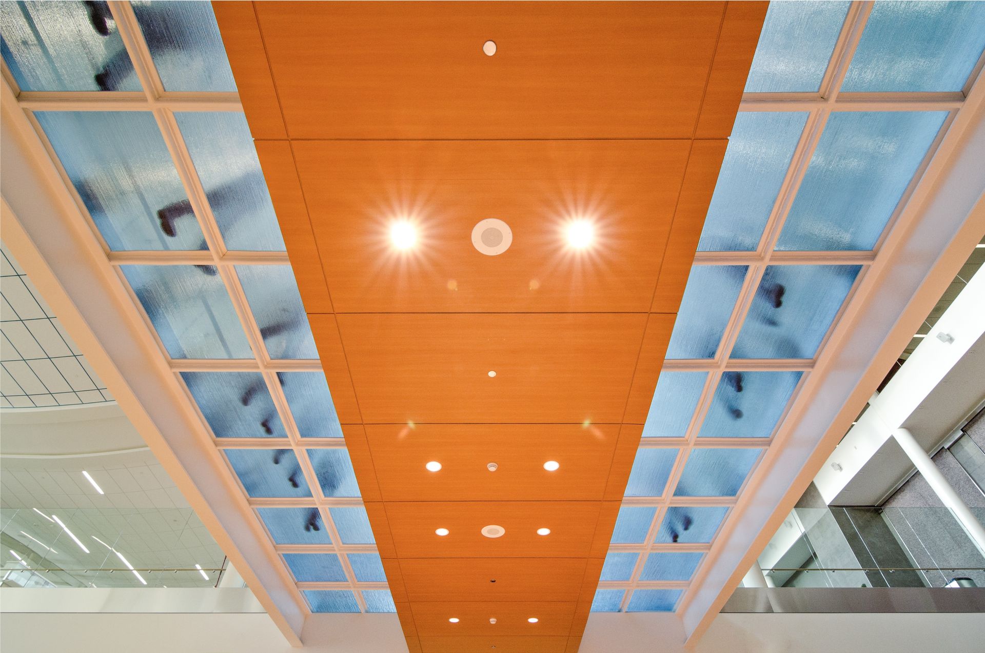 Wooden ceiling with bright lights, flanked by translucent panels showing pedestrian silhouettes.