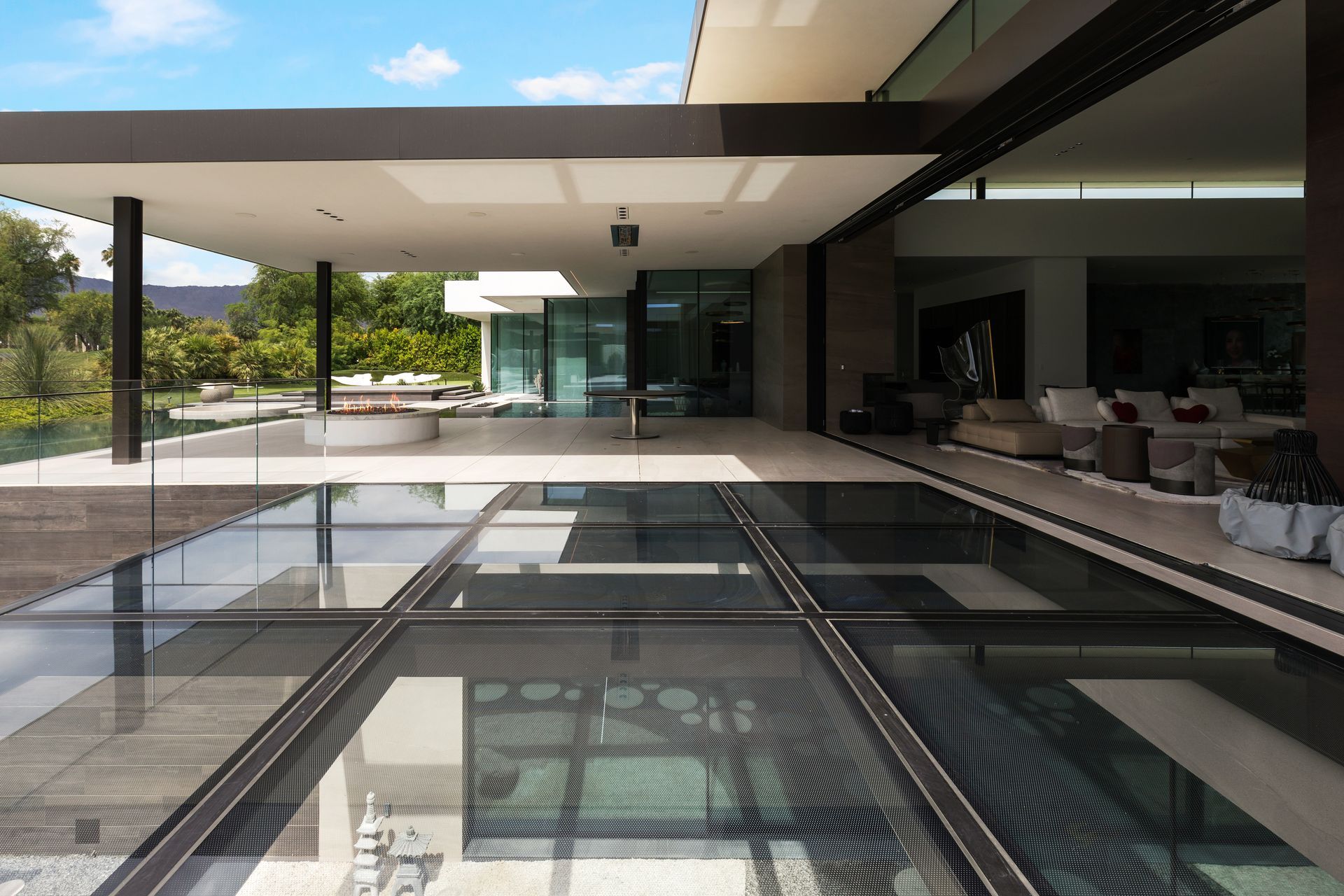 Modern house with glass floor panels, open patio, and pool in a sunny outdoor setting.