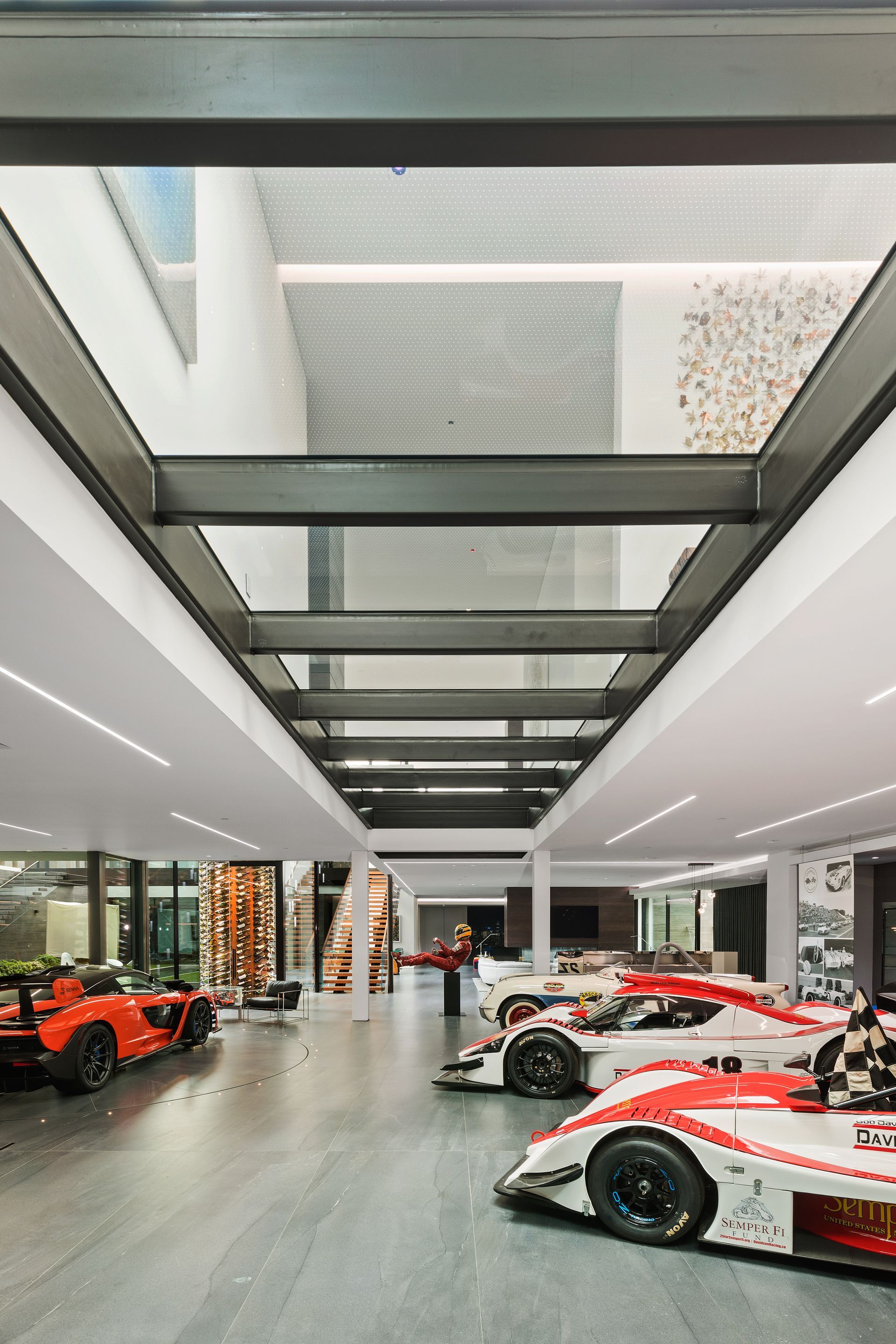 A modern garage showcasing multiple race cars; white, red, and orange against a bright interior with skylights.