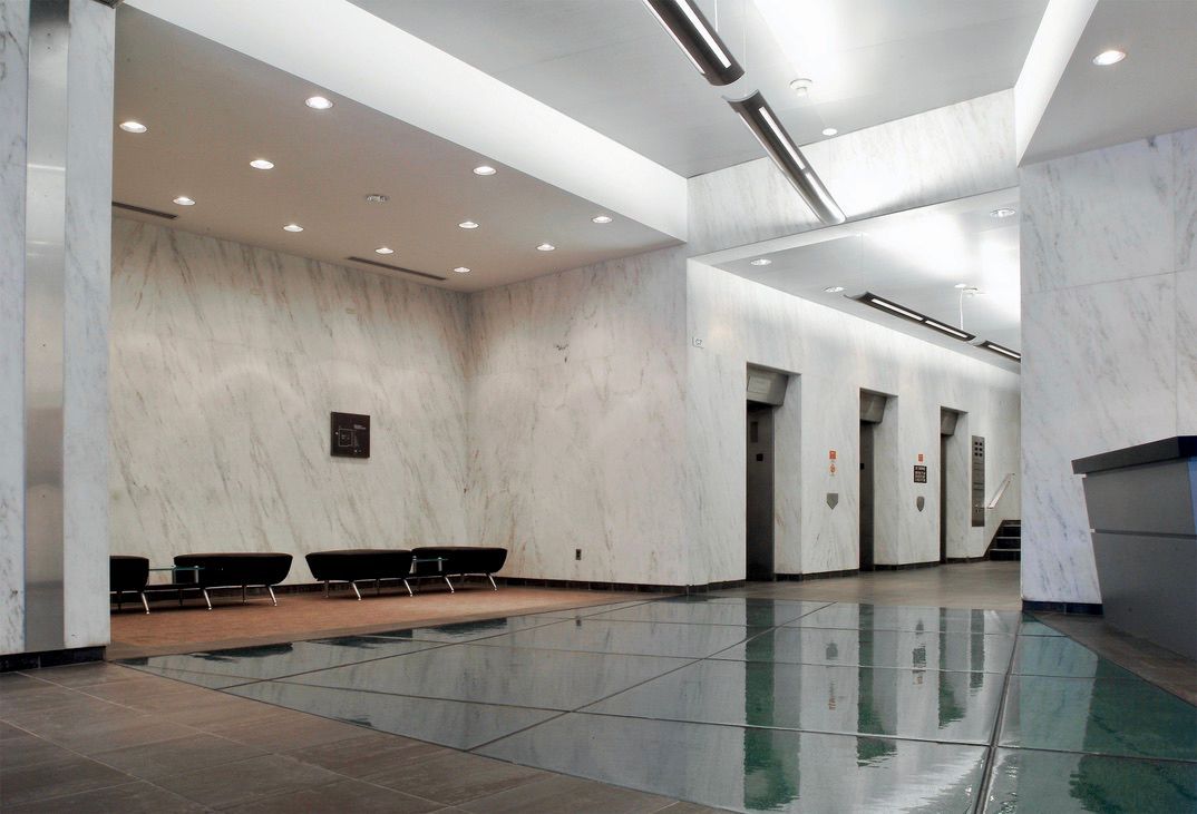 Lobby with marble walls, reflective glass floor, elevators, seating, and a reception desk.
