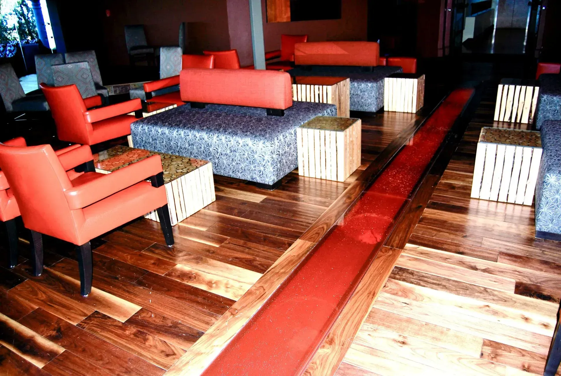 Red chairs and sofas in a lounge with wooden floors, seating around patterned and wooden tables. Red glass floor 