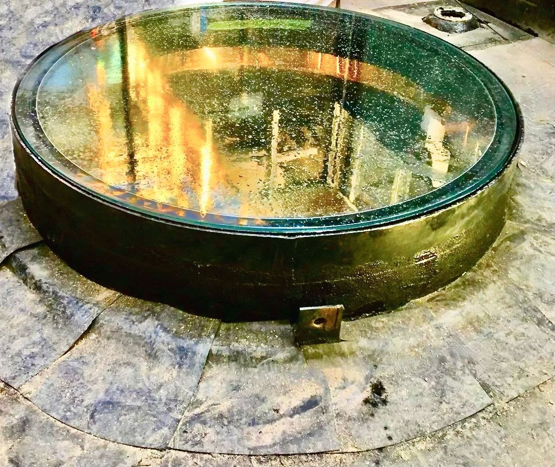 A round, glass lens set in a dark metal frame, resting on a dusty surface.