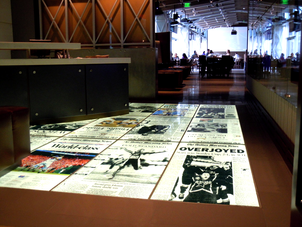 Restaurant floor with newspaper-style tile design, reflecting light. People seated in background.