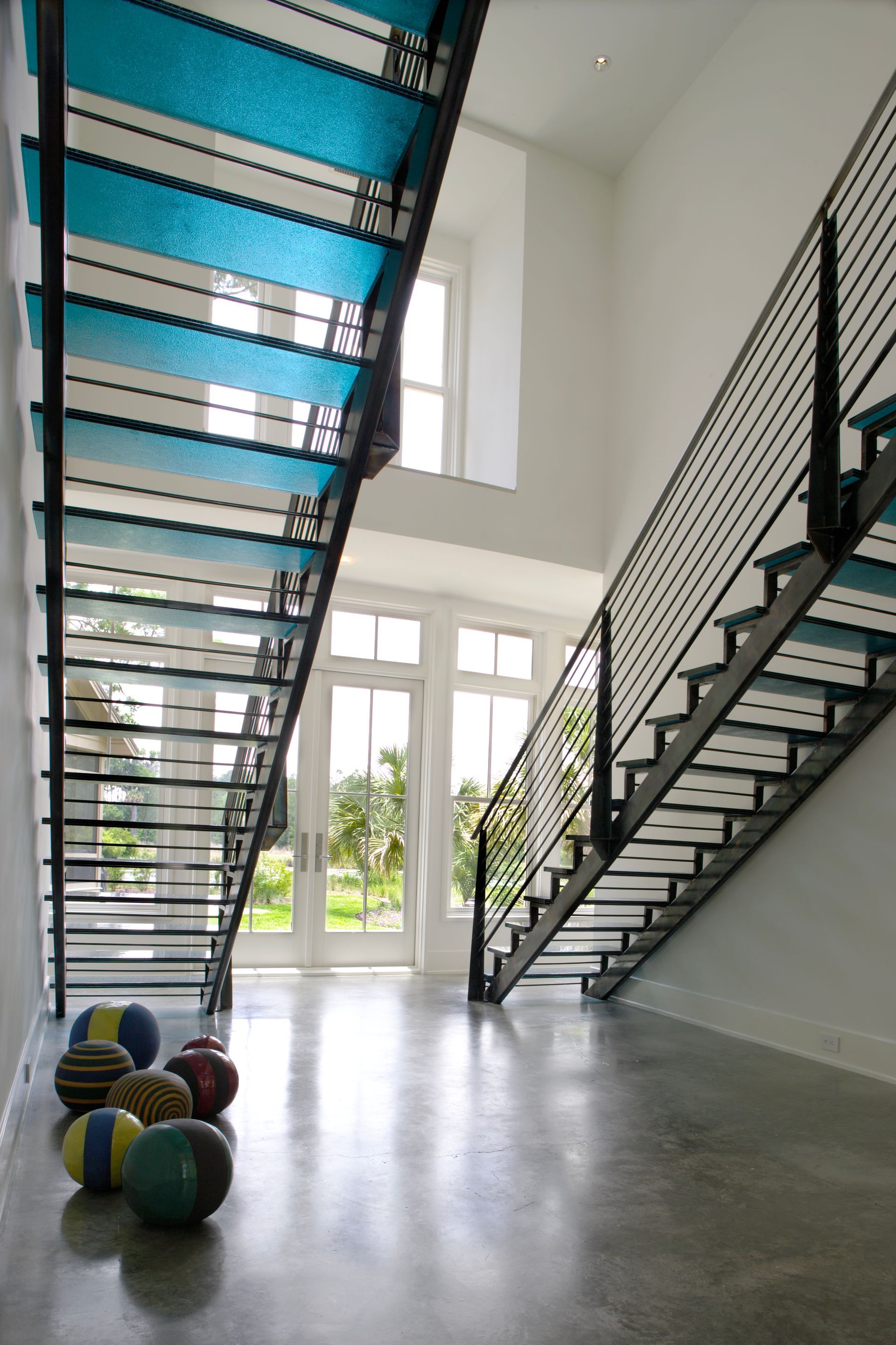 Modern staircase with turquoise treads, black railings, and a light-filled entryway. Balls in foreground.